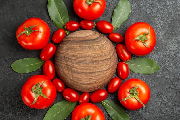 Bovenaanzicht kersen en rode tomaten laurierblaadjes rond een houten plaat op donkere grond
