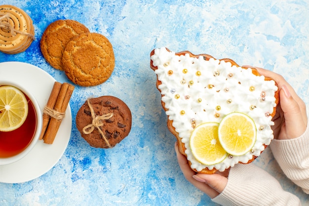 Bovenaanzicht kerstboom cake in vrouwelijke hand cookies kopje thee op blauwe tafel