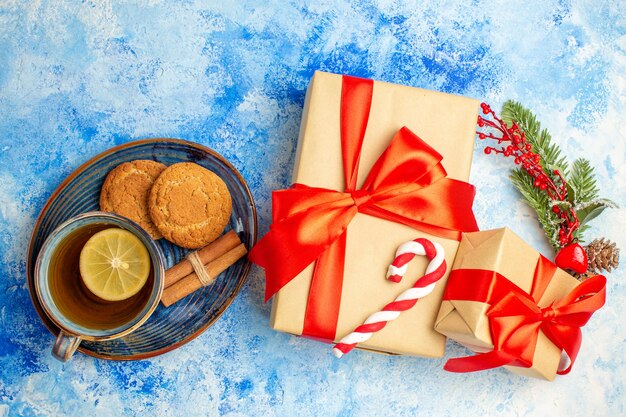 Bovenaanzicht kerstcadeaus gebonden met rode strik kopje thee koekjes kaneelstokjes op schotel op blauwe tafel