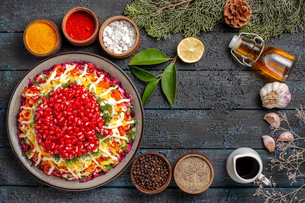 Bovenaanzicht kerstschotel met granaatappelfles olie knoflook naast de kommen met verschillende kruiden citroensparren takken met kegels op tafel