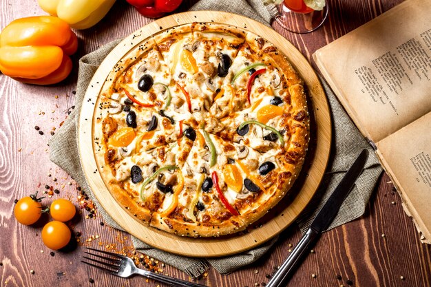Bovenaanzicht kip pizza met gele kerstomaatjes en paprika op het bord