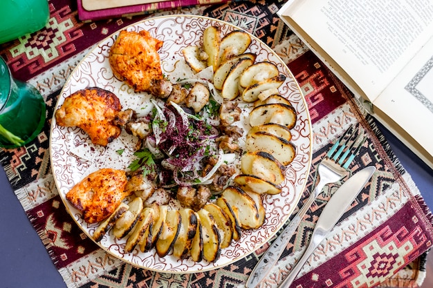 Bovenaanzicht kipbrochettes met gesneden ‹aardappelen uien en kruiden bestrooid met sumak