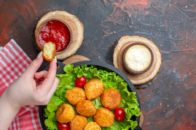 Bovenaanzicht kipnuggets en sauzen op snijplanknugget in vrouwelijke hand op donkerrode muur