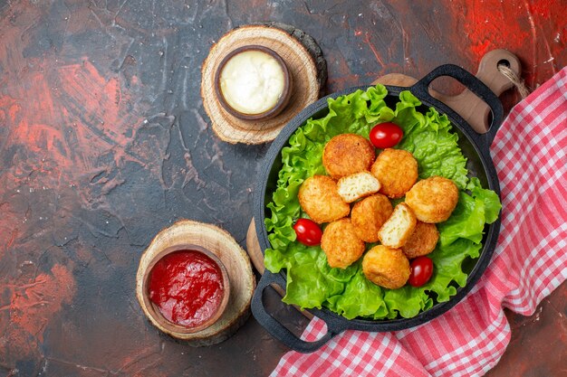 Bovenaanzicht kipnuggets in pansauskommen op houten planken op donkerrode muur met vrije ruimte