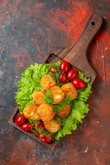 Bovenaanzicht kipnuggets sla cherrytomaatjes op een houten bord op donkere tafel