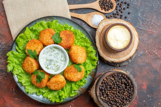 Bovenaanzicht kipnuggets sla op plaat zout en zwarte peper in houten lepels souce en zwarte peper in kommen op donkere tafel