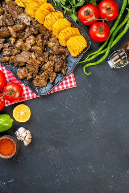 Bovenaanzicht kippenleverbak met aardappel op schotel tomaten hete groene pepers oliefles knoflook op tafel met kopieerplaats