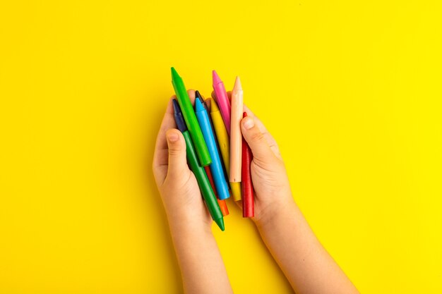 Bovenaanzicht klein kind met kleurrijke potloden op geel oppervlak