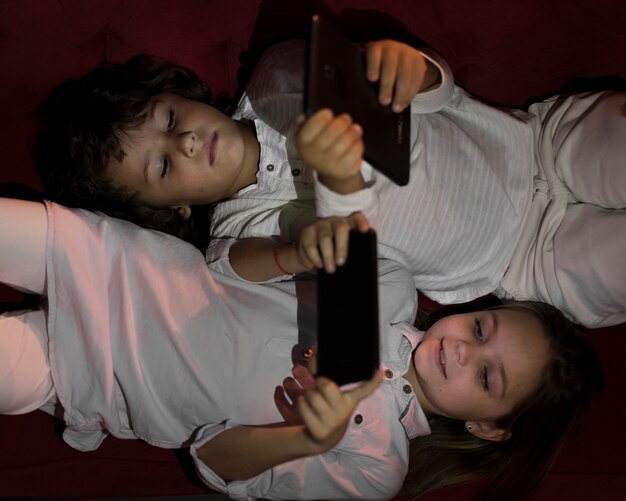 Bovenaanzicht kleine broers en zussen spelen op hun elektronische apparaten