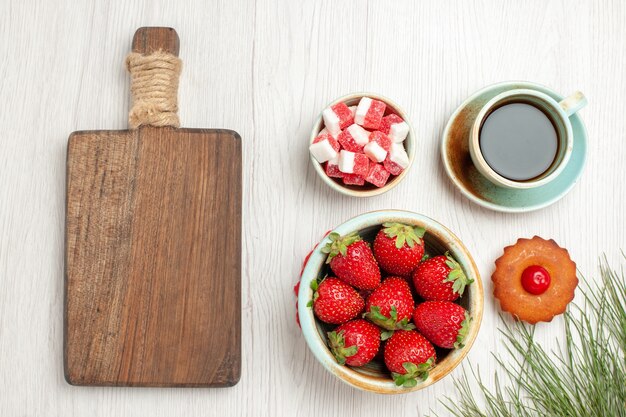 Bovenaanzicht kleine cake met fruit en kopje thee op wit bureau