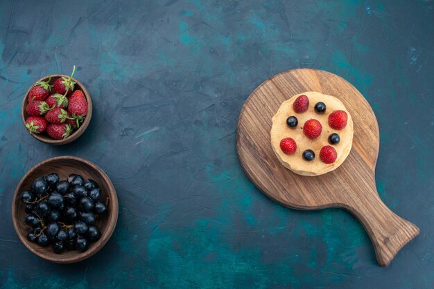 Bovenaanzicht kleine cake met verse aardbeien op het donkerblauwe oppervlak