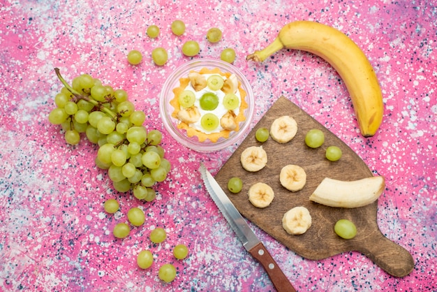 Bovenaanzicht kleine cake met verse druiven en bananen op het heldere oppervlak fruitcake frisse zachte kleur