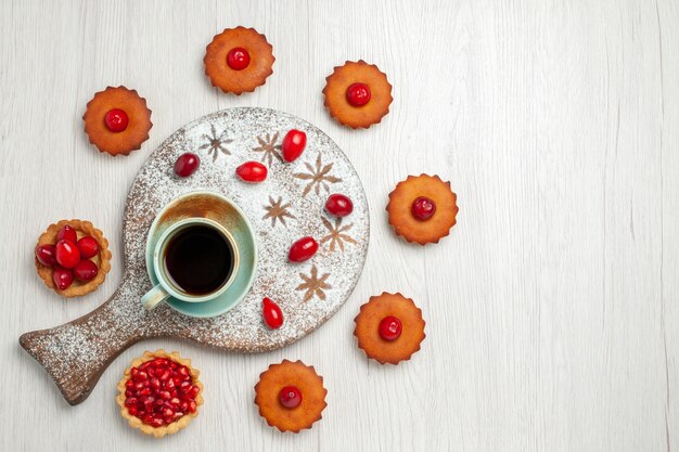 Bovenaanzicht kleine cakes met fruit en kopje thee op licht wit bureau