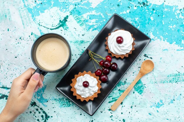 Bovenaanzicht kleine cakes met kersen en melk op de lichtblauwe bureautaart bakken zoete taartfruit