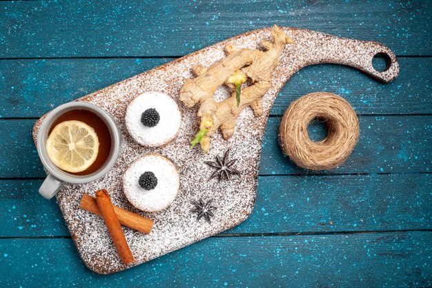 Bovenaanzicht kleine cakes met kopje thee op blauw bureau