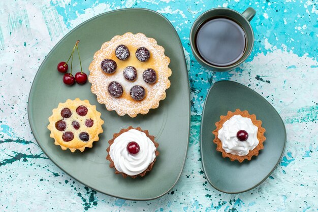 Bovenaanzicht kleine cakes met thee op de lichtblauwe tafel taart taart kersen fruit zoet