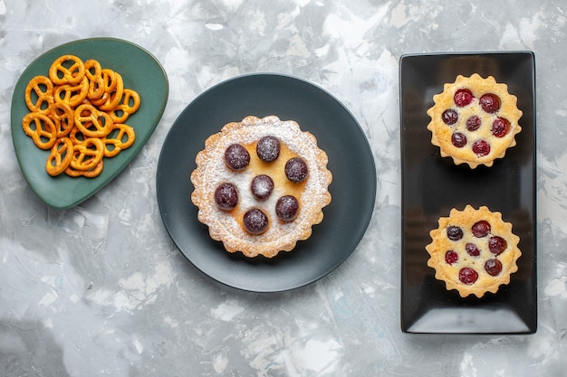 Gratis foto bovenaanzicht kleine cakes suiker gepoederd met fruit en chips op het grijze bureau fruit biscuit cake zoete suiker