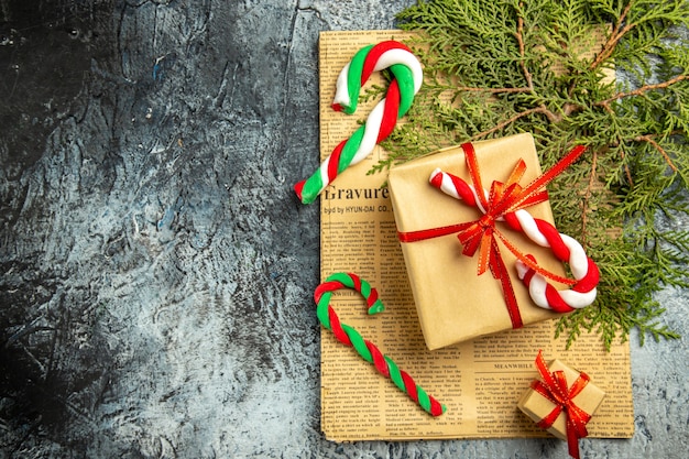 Bovenaanzicht kleine geschenken vastgebonden met rood lint kerstsnoepjes op krant pijnboomtakken op grijze achtergrond kopie ruimte