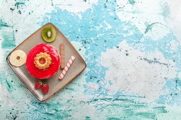 Bovenaanzicht kleine heerlijke cake met rode room op lichtblauwe achtergrond cakekoekje zoete suikertaart theekoekje