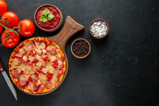 Bovenaanzicht kleine heerlijke pizza met verse rode tomaten op donkere tafel