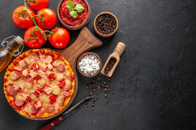 Bovenaanzicht kleine heerlijke pizza met verse rode tomaten op donkere tafel