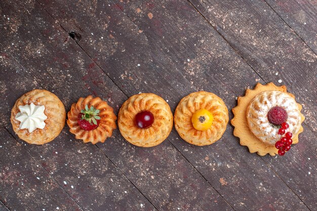 Bovenaanzicht kleine heerlijke taarten en koekjes met bessen bekleed op de bruine achtergrond cake biscuit berry foto cookie