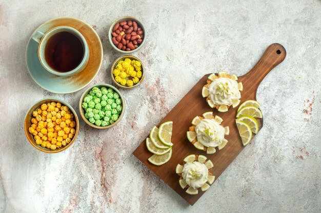 Bovenaanzicht kleine heerlijke taarten met kopje thee en snoep op wit oppervlak cake biscuit cookie zoete thee crème