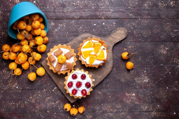 Bovenaanzicht kleine heerlijke taarten met room gesneden fruit en verse gele kersen op de bruine houten achtergrond vers fruit cake koekje zoet
