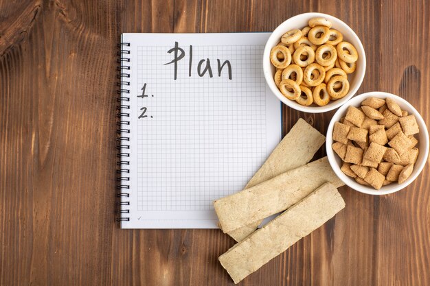 Bovenaanzicht kleine kussenkoekjes met crackers en blocnote op bruin houten bureau