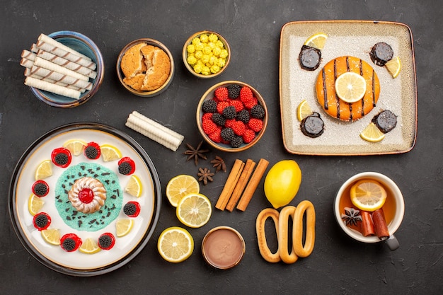 Bovenaanzicht kleine lekkere cake met schijfjes citroen en kopje thee op de donkere achtergrond biscuit fruit citrus zoete cake cookie