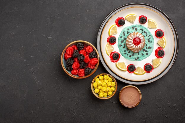 Bovenaanzicht kleine lekkere cake met schijfjes citroen en snoepjes op donkere achtergrond, fruit, citruskoekjeskoekje, zoet