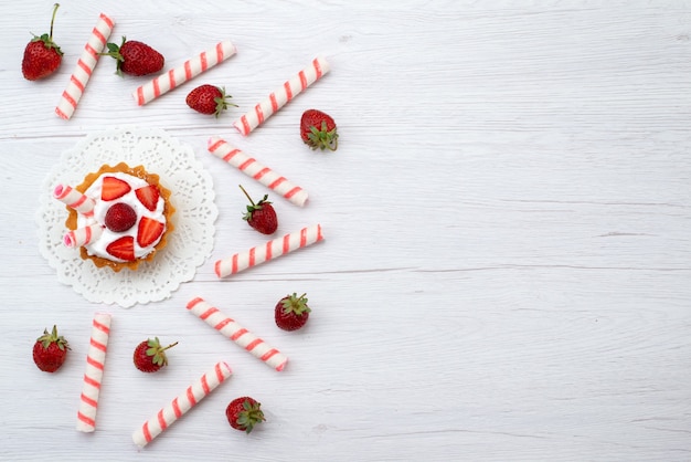 Bovenaanzicht kleine lekkere cakes met room en gesneden aardbeien snoepjes op de witte achtergrond cake bessen zoet bakken