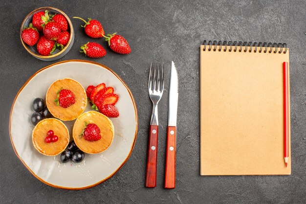 Bovenaanzicht kleine lekkere pannenkoeken met fruit op donkergrijs desk pie cake fruit