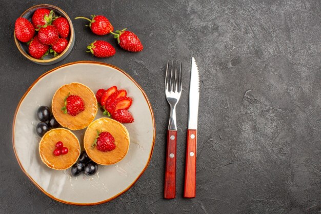 Bovenaanzicht kleine lekkere pannenkoeken met fruit op het donkergrijze oppervlak taartcake fruit