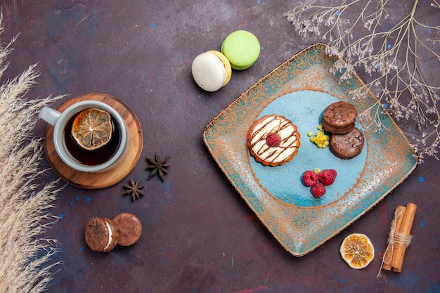 Bovenaanzicht kleine romige cake met chocoladekoekjes en kopje thee op het donkere oppervlak biscuit zoete taart suiker koekjes cake