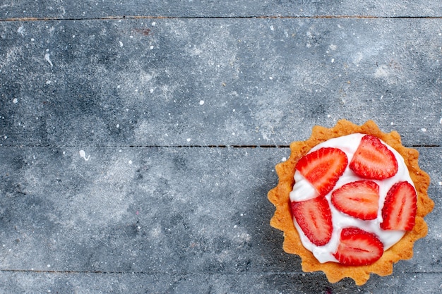 Bovenaanzicht kleine romige cake met gesneden aardbeien op de grijze achtergrond bureau fruitcake zoete kleur