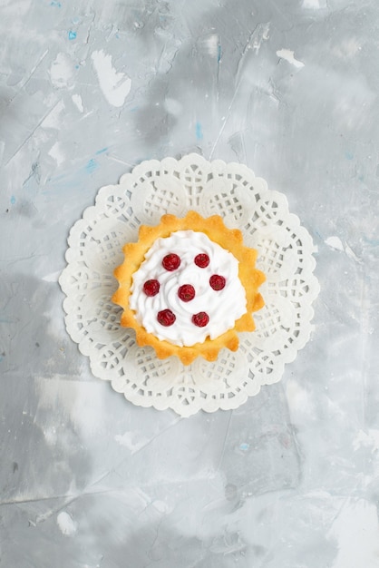 Bovenaanzicht kleine romige cake met rood fruit op de grijze oppervlakte zoete room