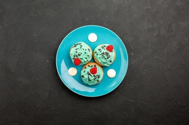 Bovenaanzicht kleine romige taarten heerlijke snoepjes voor thee binnen plaat op donkere oppervlakte crème cake biscuit dessert thee kleur