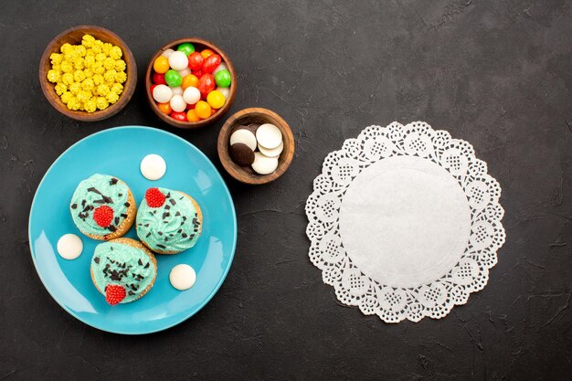 Bovenaanzicht kleine romige taarten met snoepjes op donkere oppervlakte dessert cake biscuit kleur snoep crème