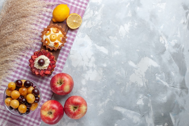 Bovenaanzicht kleine romige taarten met verse rode appels op wit bureau fruitcake koekjesroom zoet