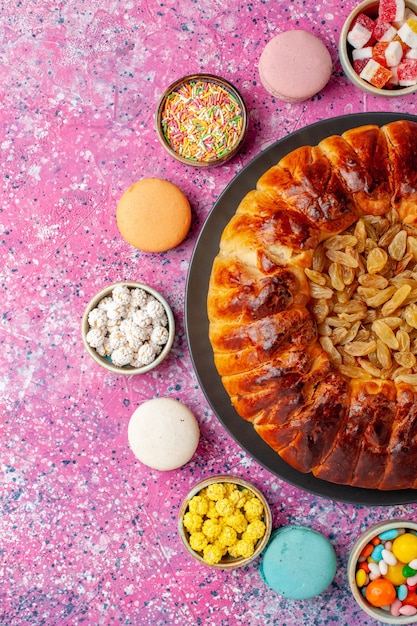 Bovenaanzicht kleurrijke franse macarons kleine heerlijke cakes met snoepjes en rozijntaart op het roze bureau suiker bak biscuit koekjes cake taart