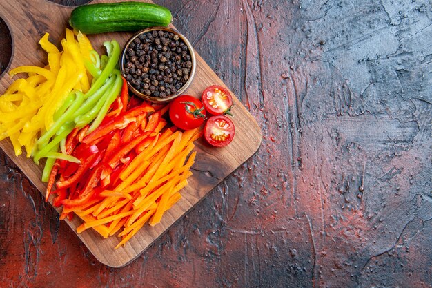 Bovenaanzicht kleurrijke gesneden paprika zwarte peper tomaten komkommer op snijplank op donkerrode tafel met kopie ruimte