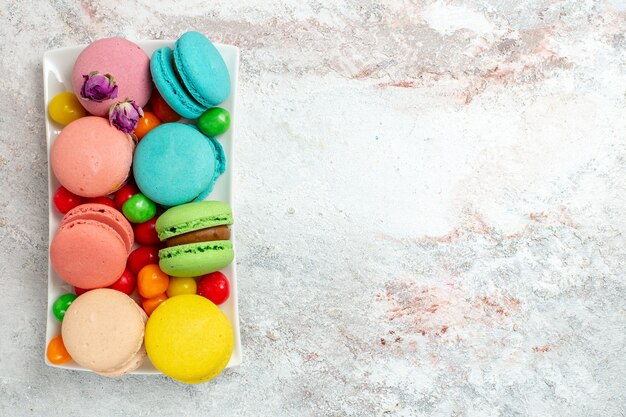Bovenaanzicht kleurrijke heerlijke macarons kleine cakes met snoepjes op witte ruimte