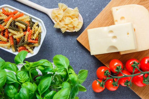 Bovenaanzicht kleurrijke macaroni pasta in kom met tomaten, bladeren, kaas op grijze ondergrond. horizontaal