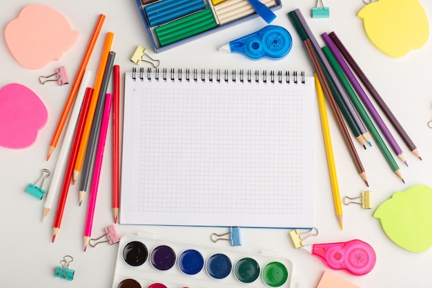 Bovenaanzicht kleurrijke potloden met verf Kladblok en stickers op wit bureau kunst tekening kleur verf