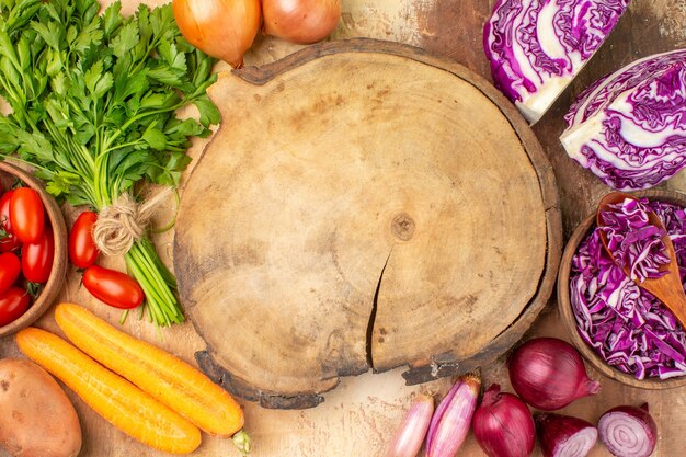 Bovenaanzicht kleurrijke salade ingrediënten gemaakt van een bosje rode kool peterselie roma tomaten wortel aardappelen en uien rond een snijplank op een houten achtergrond met ruimte voor tekst