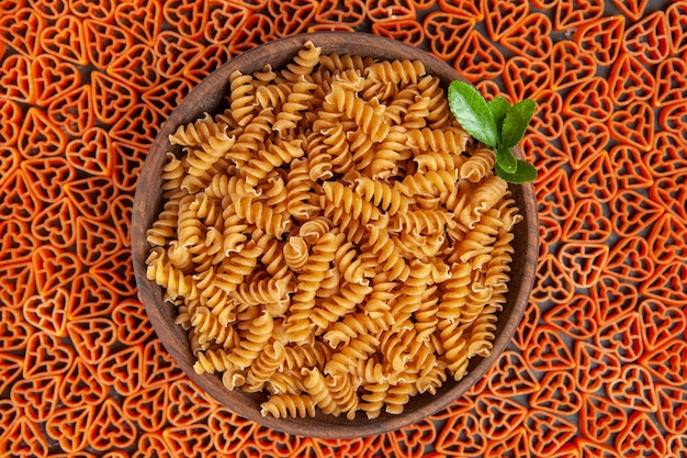 Gratis foto bovenaanzicht kom met spirali pasta op hartvormige italiaanse pasta op donkere tafel