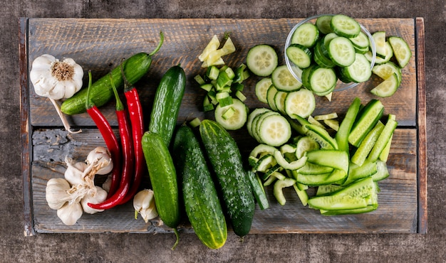 Bovenaanzicht komkommer gesneden op houten snijplank met chili peper en knoflook op bruine houten