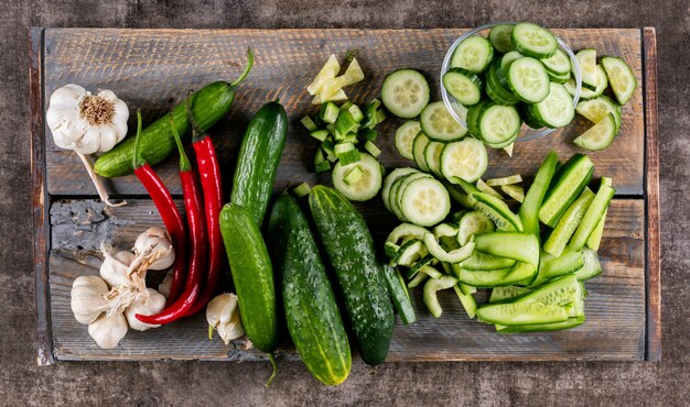 Bovenaanzicht komkommer gesneden op houten snijplank met chili peper en knoflook op bruine houten