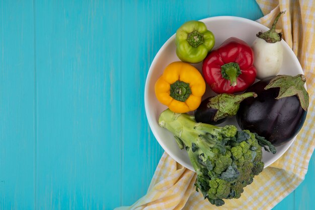 Bovenaanzicht kopie ruimte gekleurde paprika met broccoli en aubergine op een bord met een gele geruite handdoek op een turkooizen achtergrond